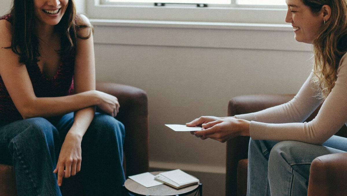 Zwei Frauen sitzen sich gegenüber und vergleichen ihre Wertekarten, Werte-Test für Paare
