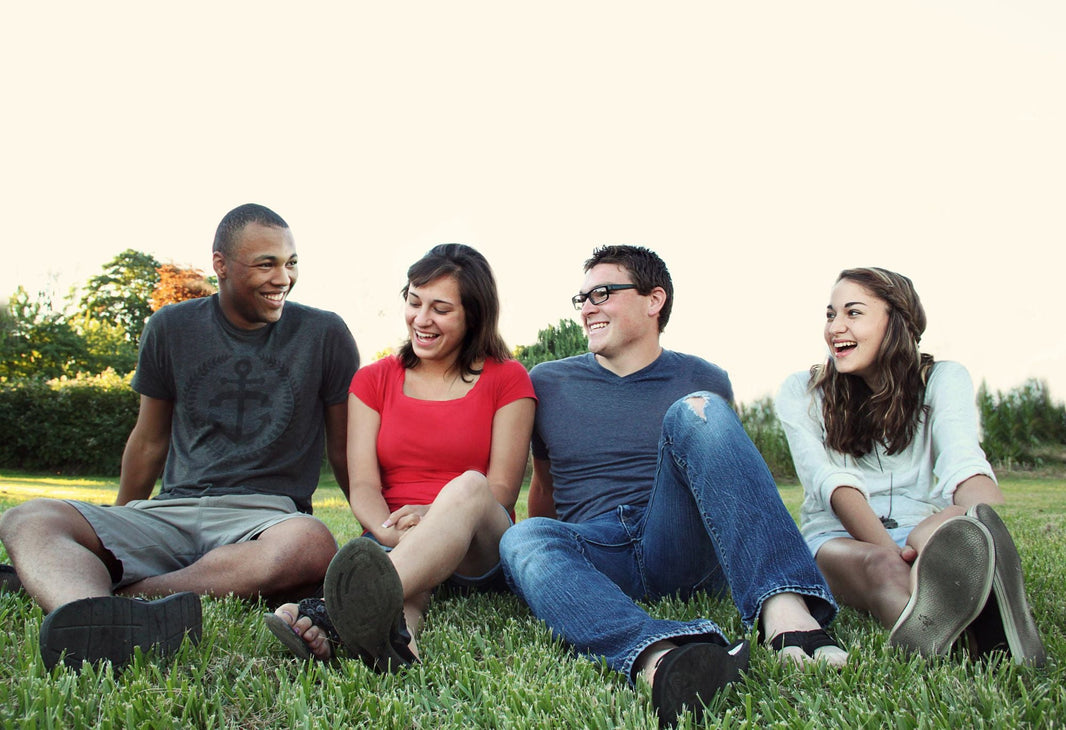 Junge Freunde sitzen lachend zusammen im Park auf dem Gras