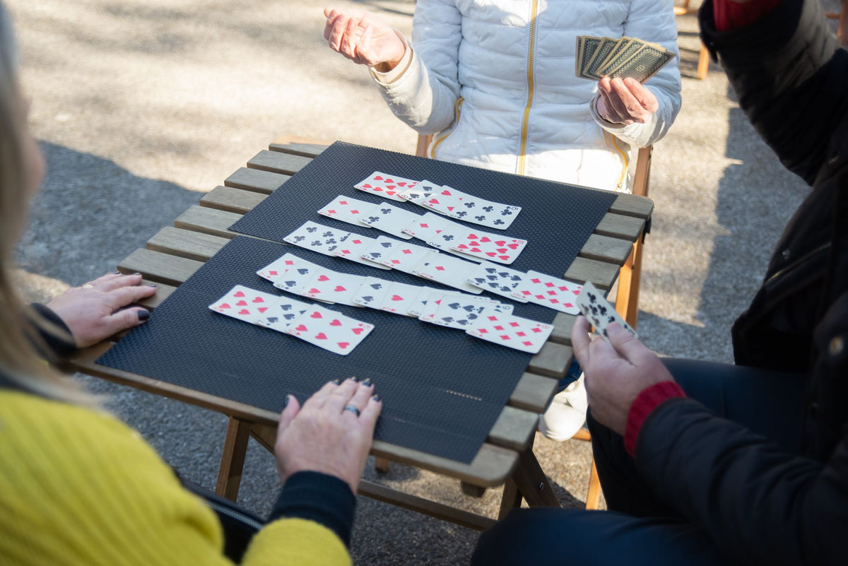 Menschen spielen draußen gemeinsam Karten am Tisch