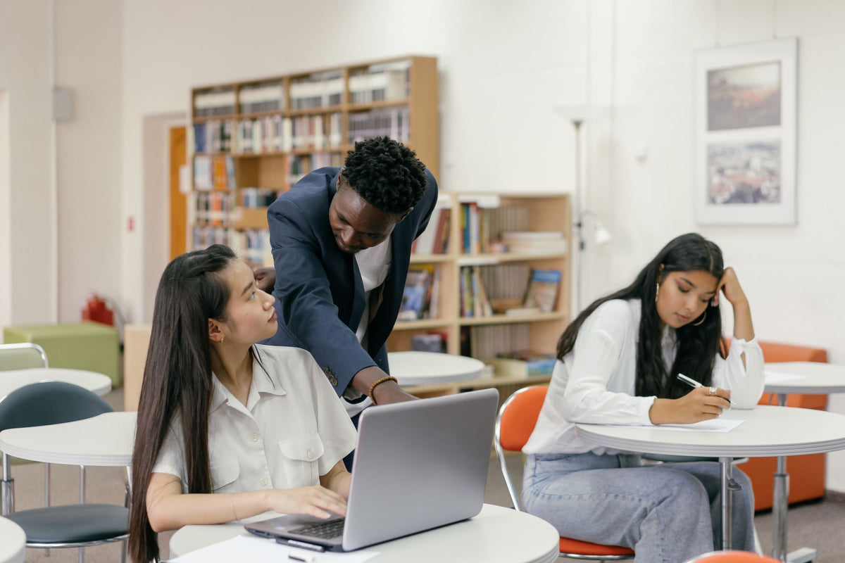 Lehrer hilft Schülerinnen an ihren Plätzen im Klassenzimmer